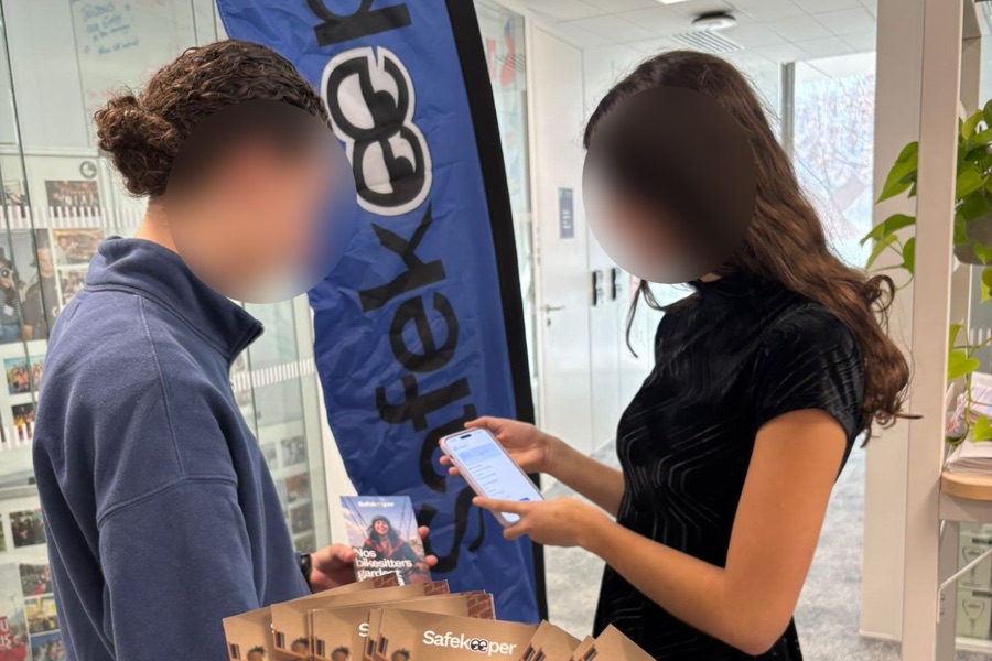 Stand Safekeeper sur le campus d'emlyon : une ambassadrice présente l'application sur son téléphone à une étudiante, devant le kakémono de la marque et les flyers « Nos bikesitters gardent ».